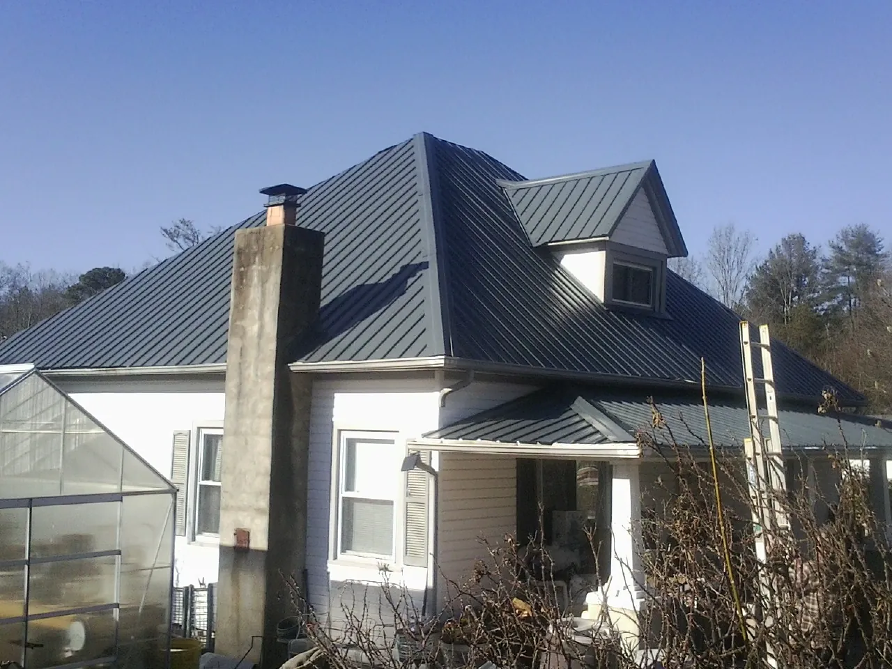 Dark blue standing seam metal roof on a white farmhouse with dormer — Slate & Tile Roof Repair by Roofing Brothers in Afton