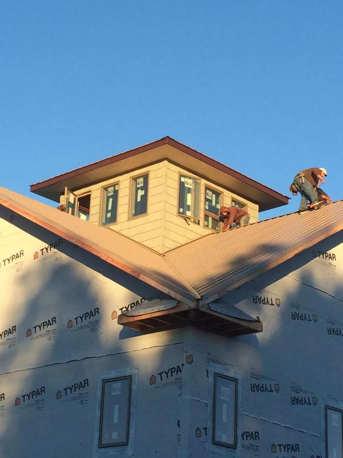 Roofers working around a rooftop cupola on a new metal roof at sunset — Roof Waterproofing in Afton by Roofing Brothers